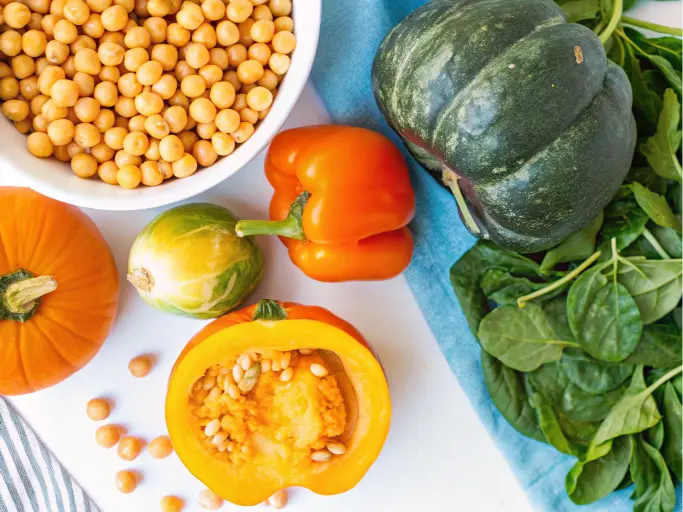 A colorful assortment of vegetables including kabocha squash, pumpkins, bell peppers, and leafy greens.