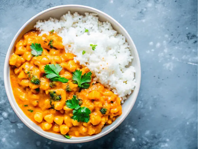 A bowl of creamy kabocha squash curry served over white rice, garnished with fresh parsley